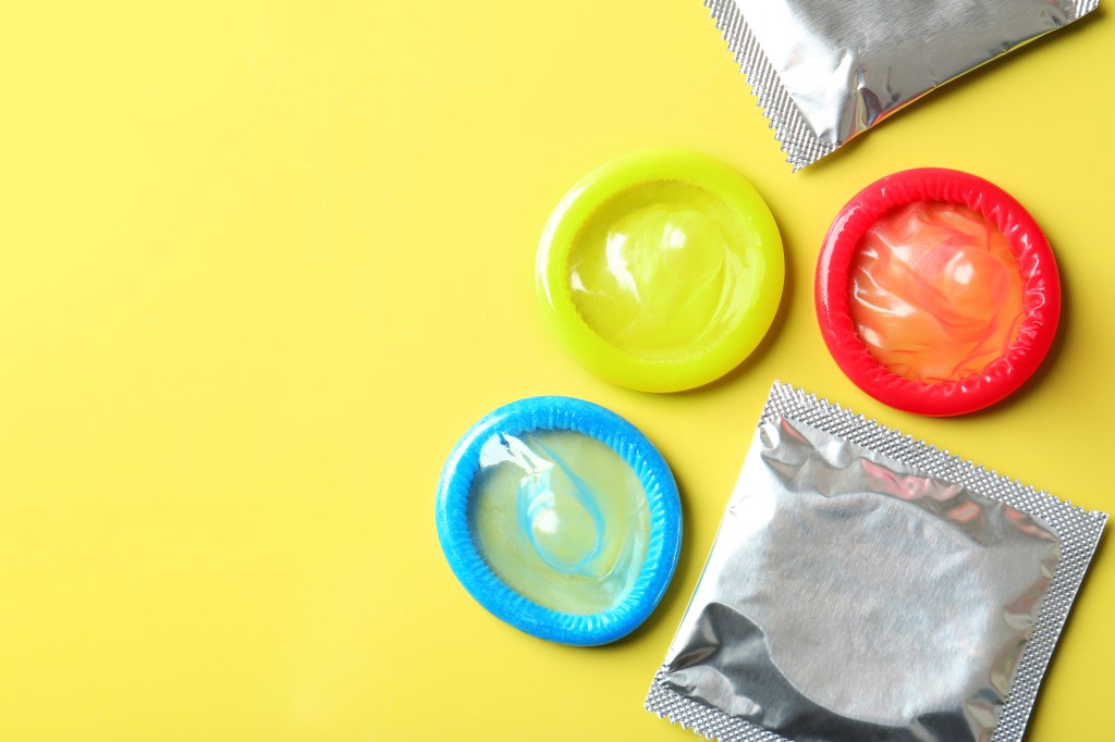 Opened and wrapped condoms on colored background